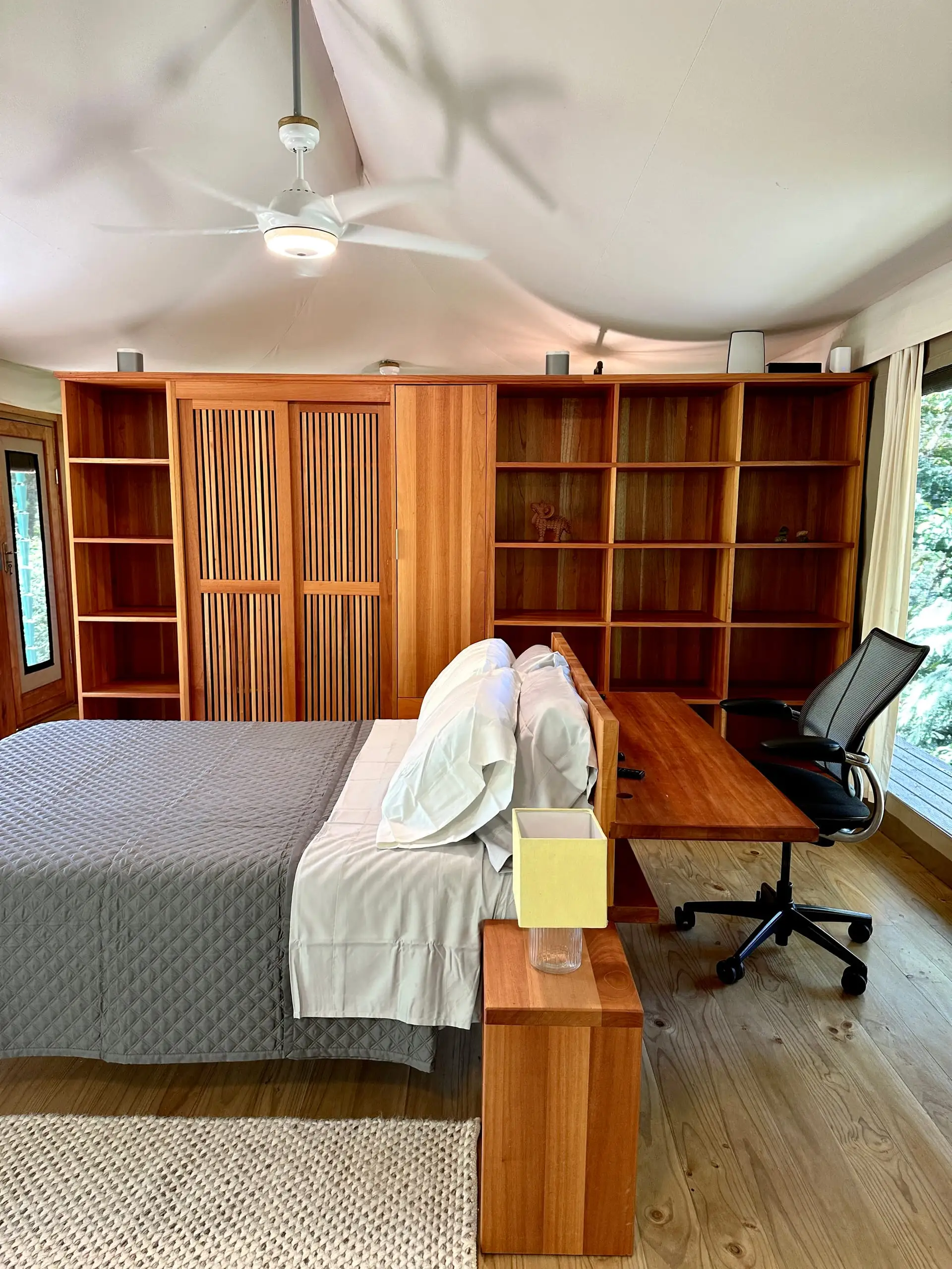 The bed and writing desk against the full-height shelving wall