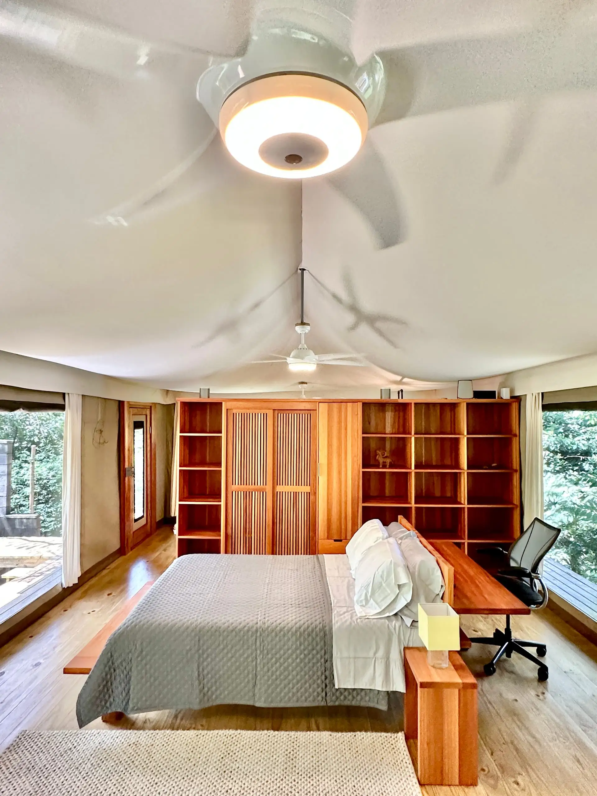 The bed beneath the tent’s sculptural canvas ceiling, framed by a wall of handmade hardwood shelving