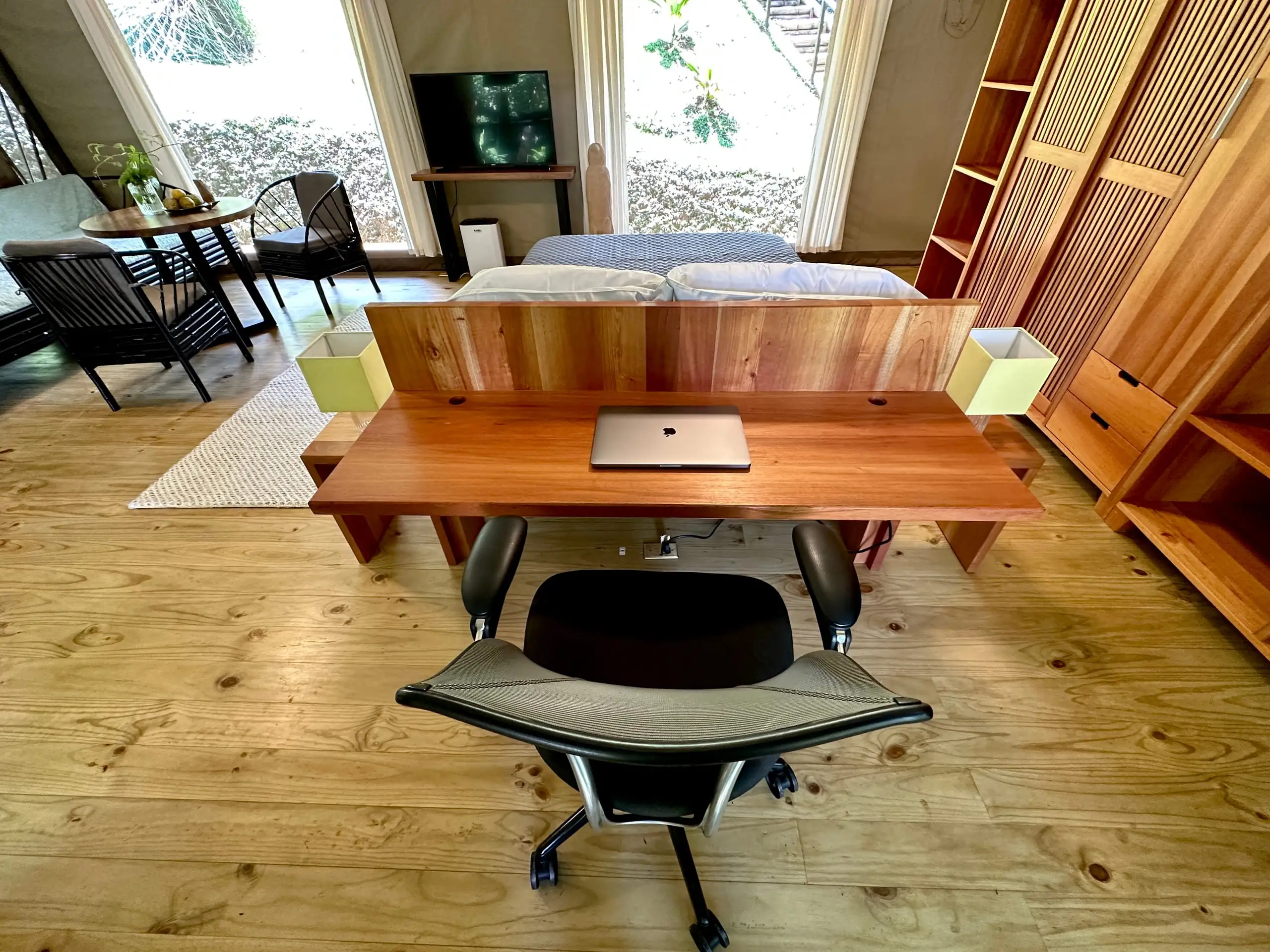 The desk set up for working, laptop open, jungle beyond