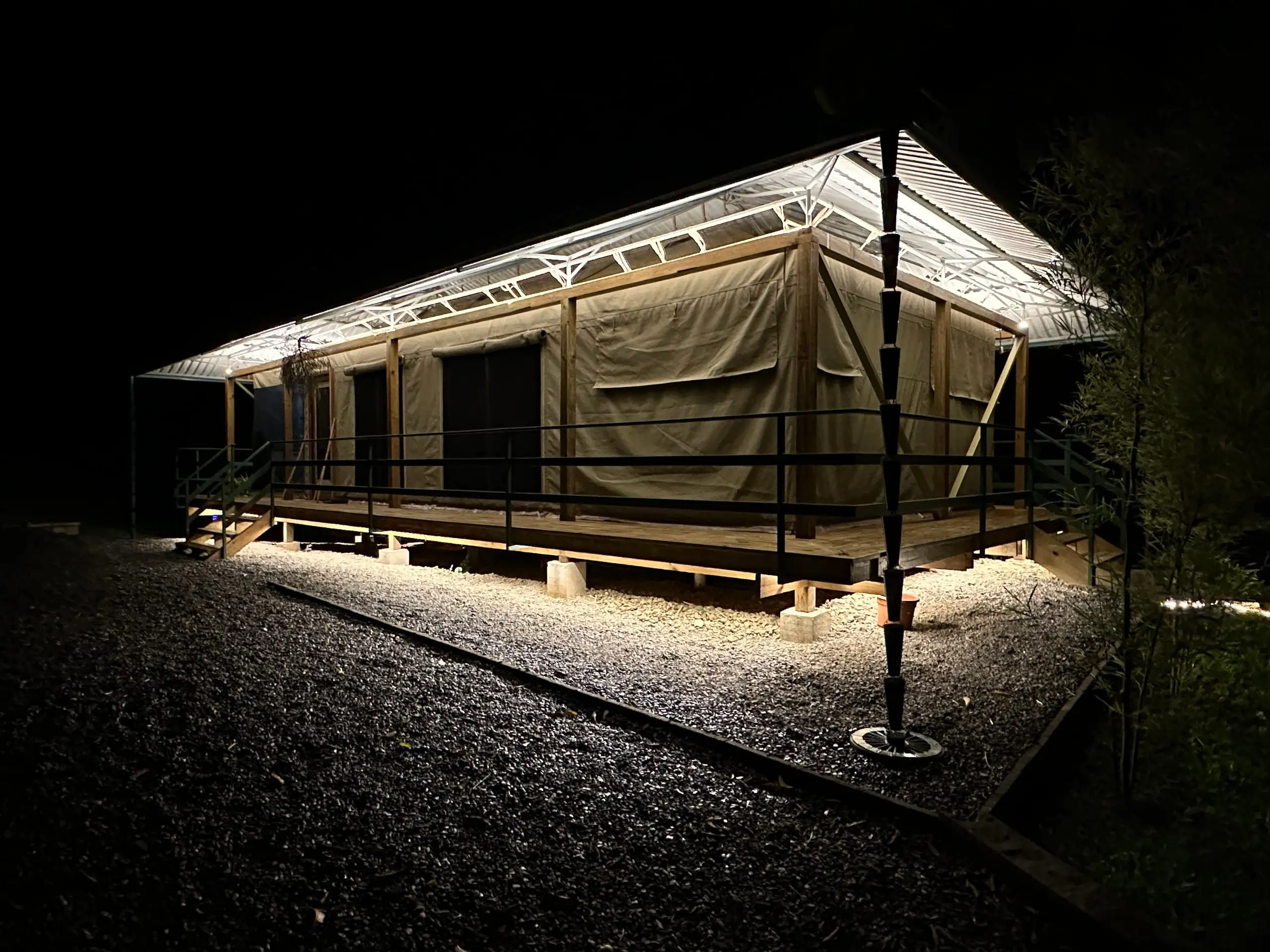 The tent at dusk, canvas lit from within and the deck underlit, the roofline lost against the sky