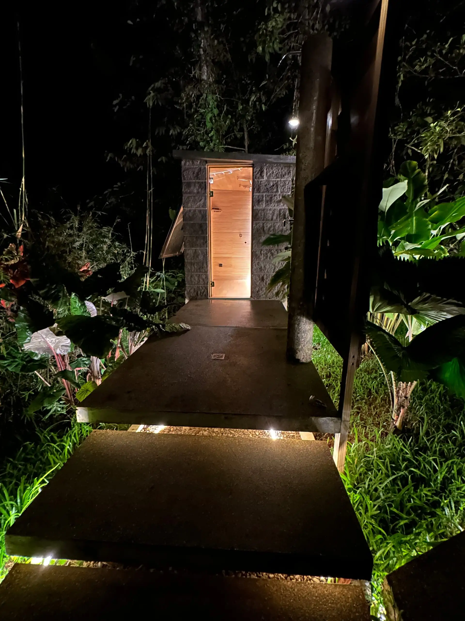 The steam room lit from within at night, a glowing doorway in dark jungle